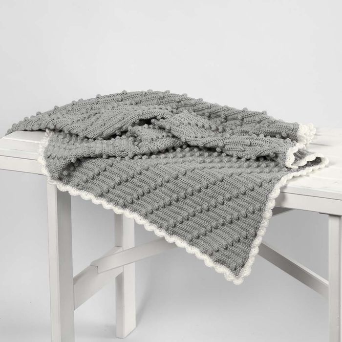 Una coperta per bebè all'uncinetto con piccoli pom pom diagonali