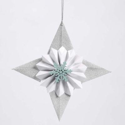 Una stella di carta glitter con una coccarda e un fiocco di neve